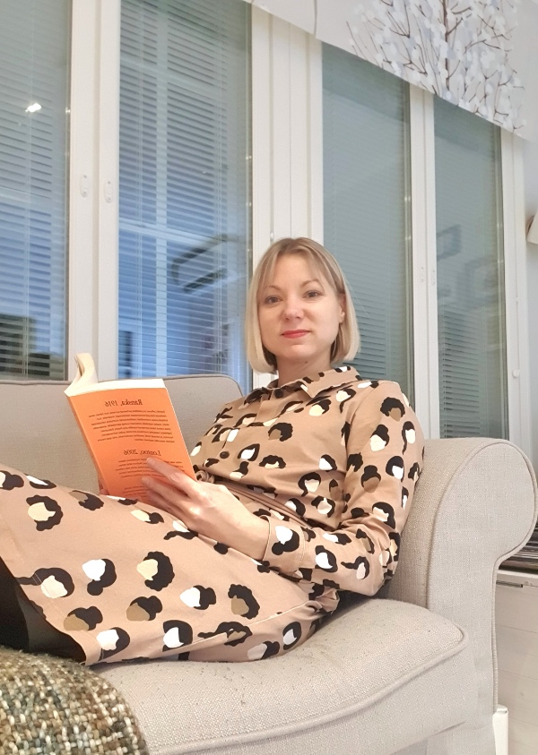 Ametron kotisiivouksen asiakas Tiia Rouhiainen istuu sohvalla ja lukee kirjaa.